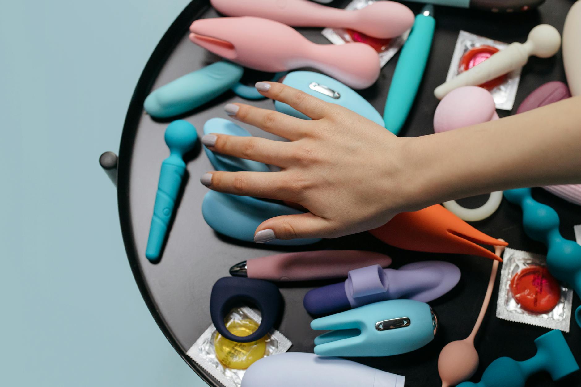 Woman holding colorful vibrators thoughtfully against a neutral background